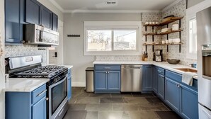 Cozinha moderna com armários azuis, eletrodomésticos de aço inoxidável e uma janela que proporciona iluminação natural.
