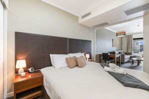 A hotel room with a large bed, a desk, a chair, and a view of the city. - Top Floor Tropical Escape | Pool | King Bed | Balcony (Darwin City)