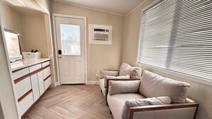 A room with a herringbone floor, a beige sofa, a white door, and a window with blinds. - Golf House Retreat-Newly Remodeled 4BR (Tempe)