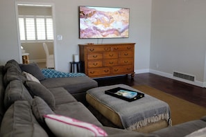 Ein Wohnzimmer mit Ecksofa, einer Holzkommode, einem Flachbildfernseher und einem kleinen Tisch mit Tablett.