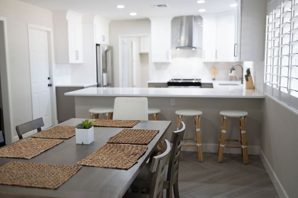 A modern kitchen with white cabinets, a stainless steel range hood, and a central island with stools.