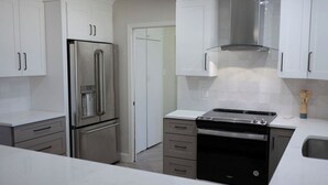A modern kitchen with stainless steel appliances, white cabinetry, and a black oven. - Golf House Retreat-Newly Remodeled 4BR (Tempe)