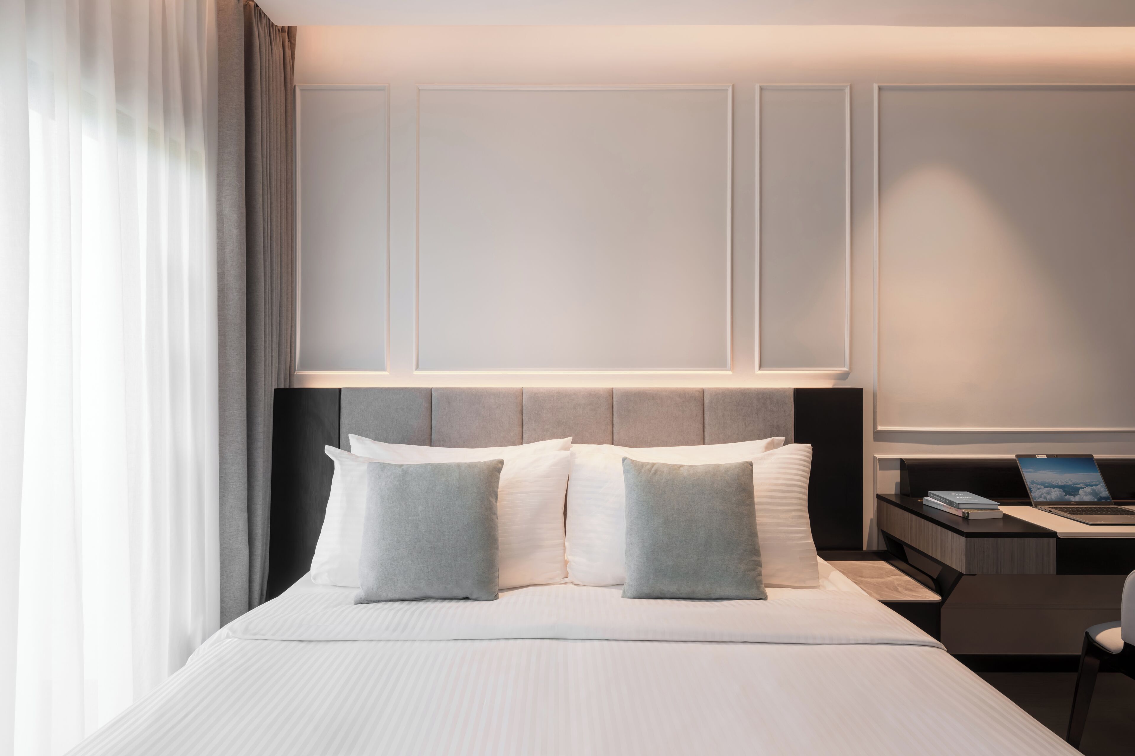 Una habitación de hotel moderna con una cama grande, un escritorio con una computadora portátil y una mesita de noche.