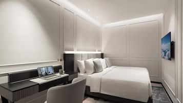A modern hotel room with a bed, desk, chair, and a flat-screen TV mounted on the wall.