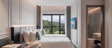 Habitación de hotel moderna con una cama grande, un escritorio, una silla, un baño y un balcón con vistas a la vegetación.