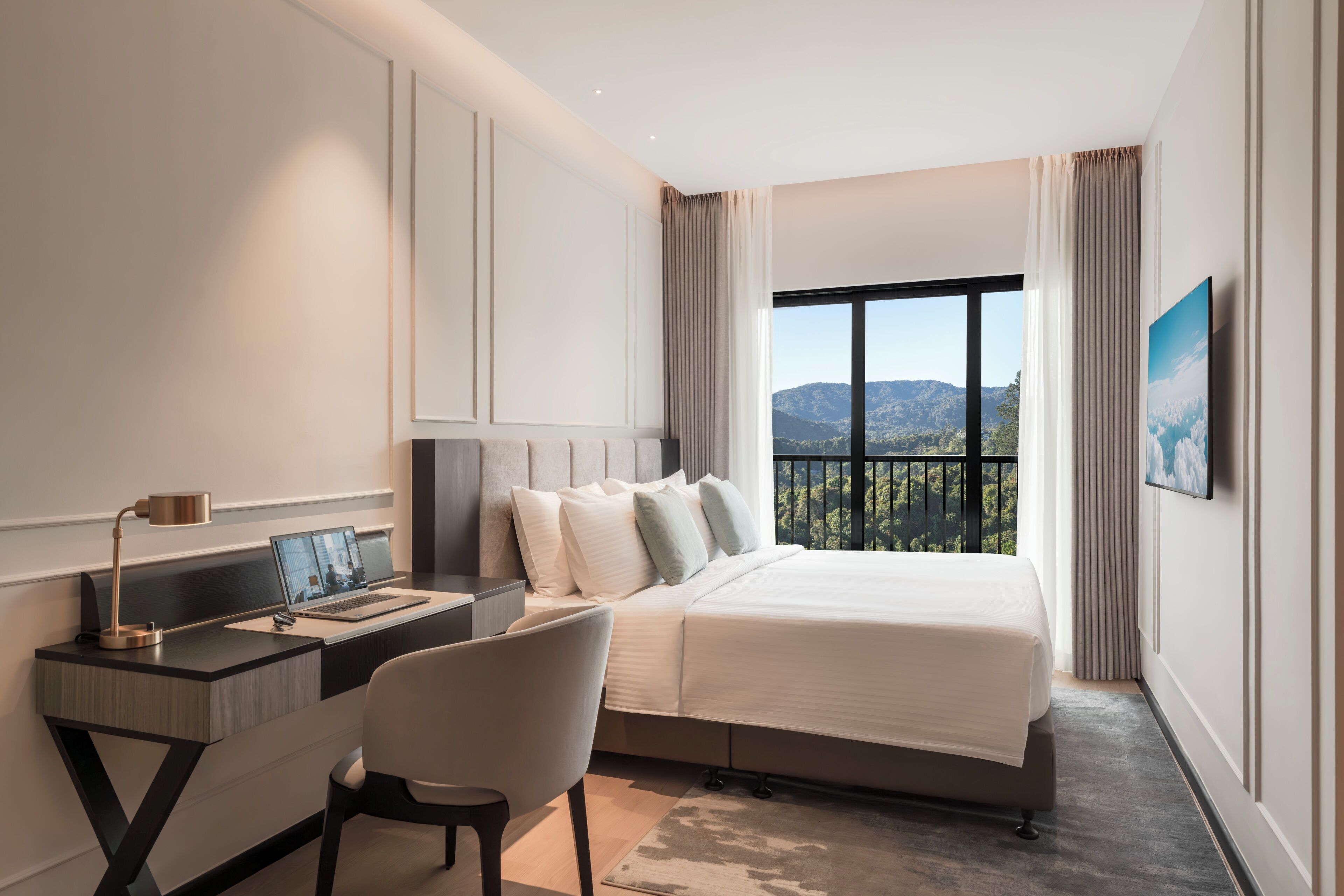 A modern hotel room with a bed, desk, chair, and a large window offering a mountain view.