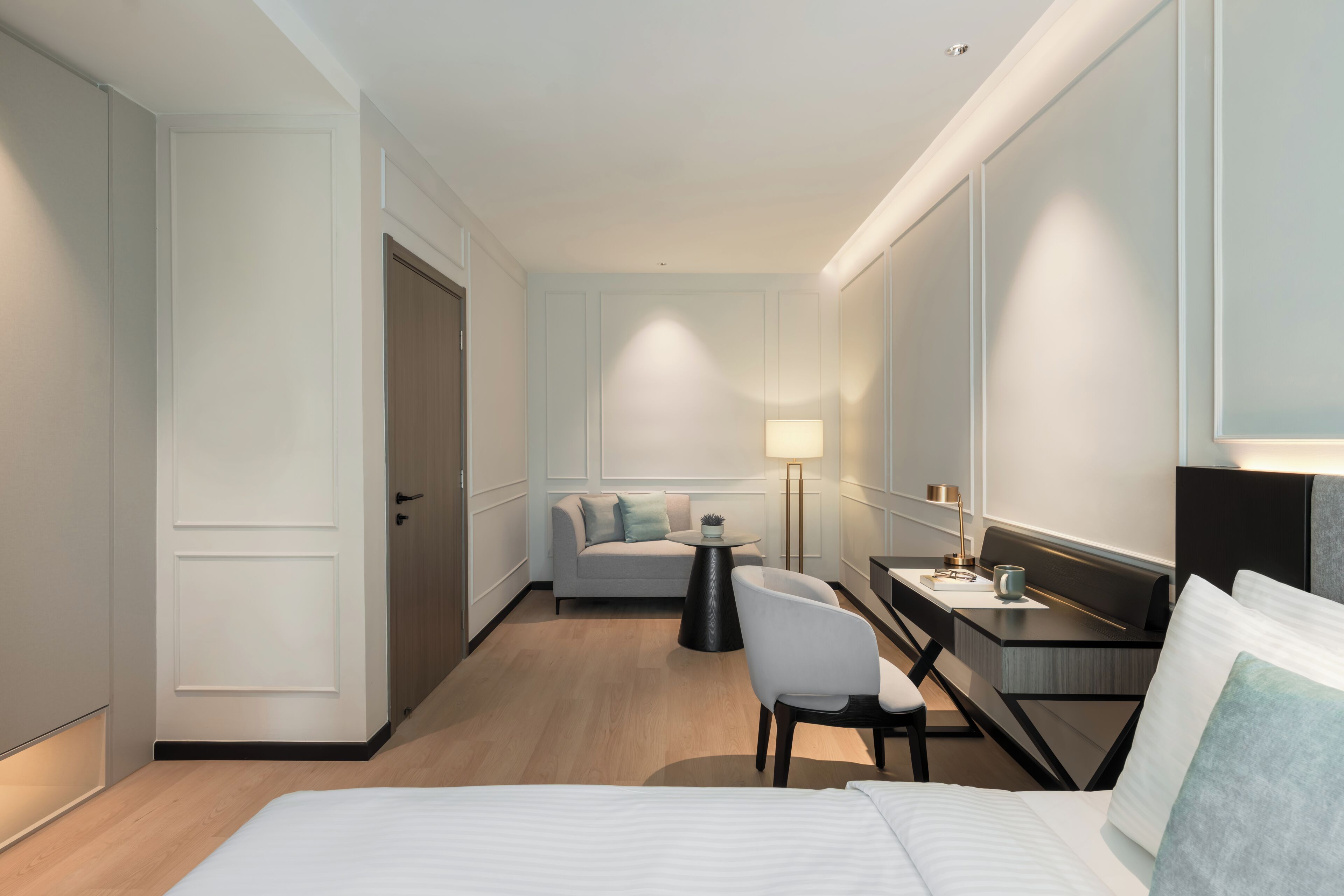 A hotel room with a bed, a desk, a chair, a sofa, and a lamp.