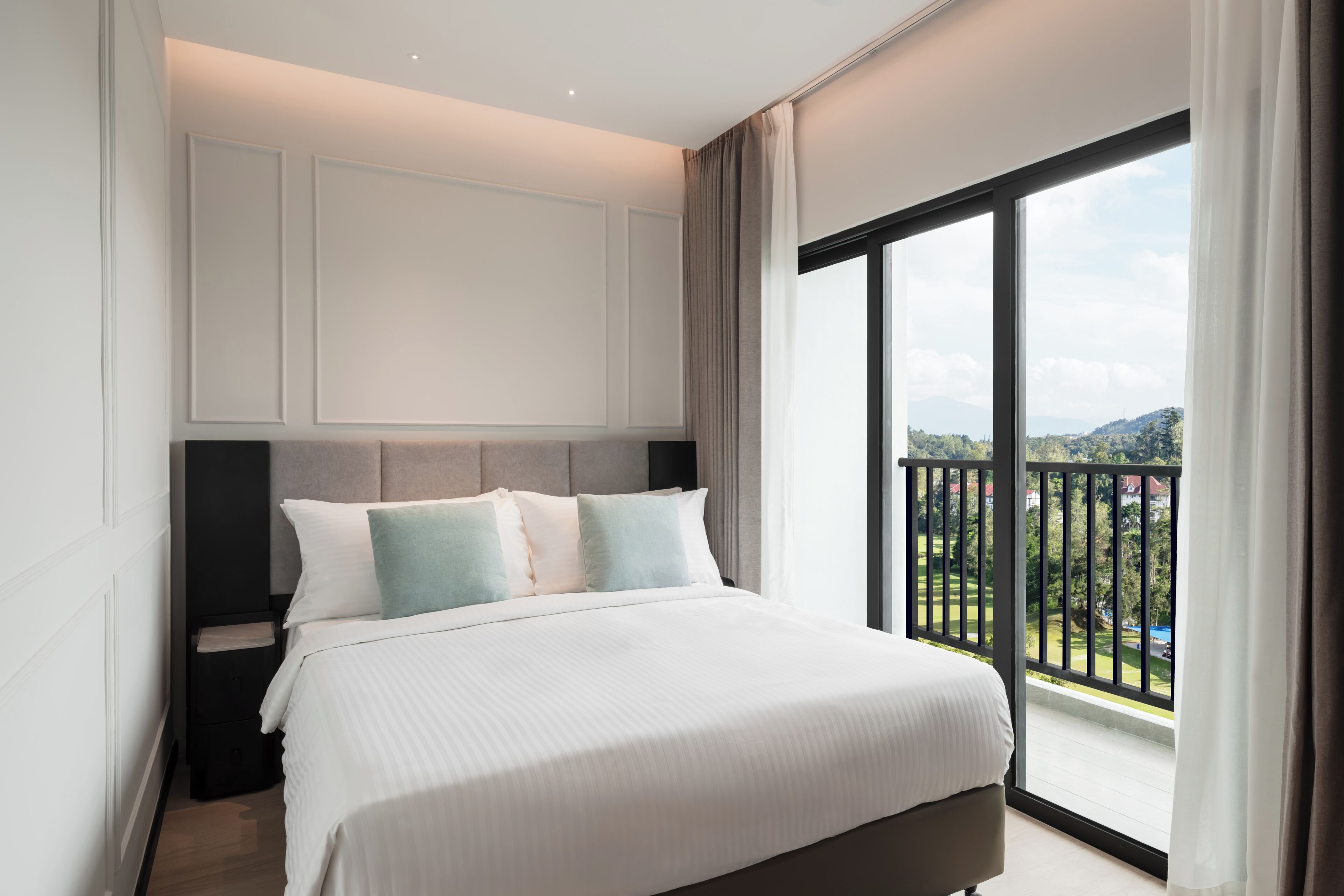 A bedroom with a large bed, a headboard, a nightstand, and a view of a balcony.