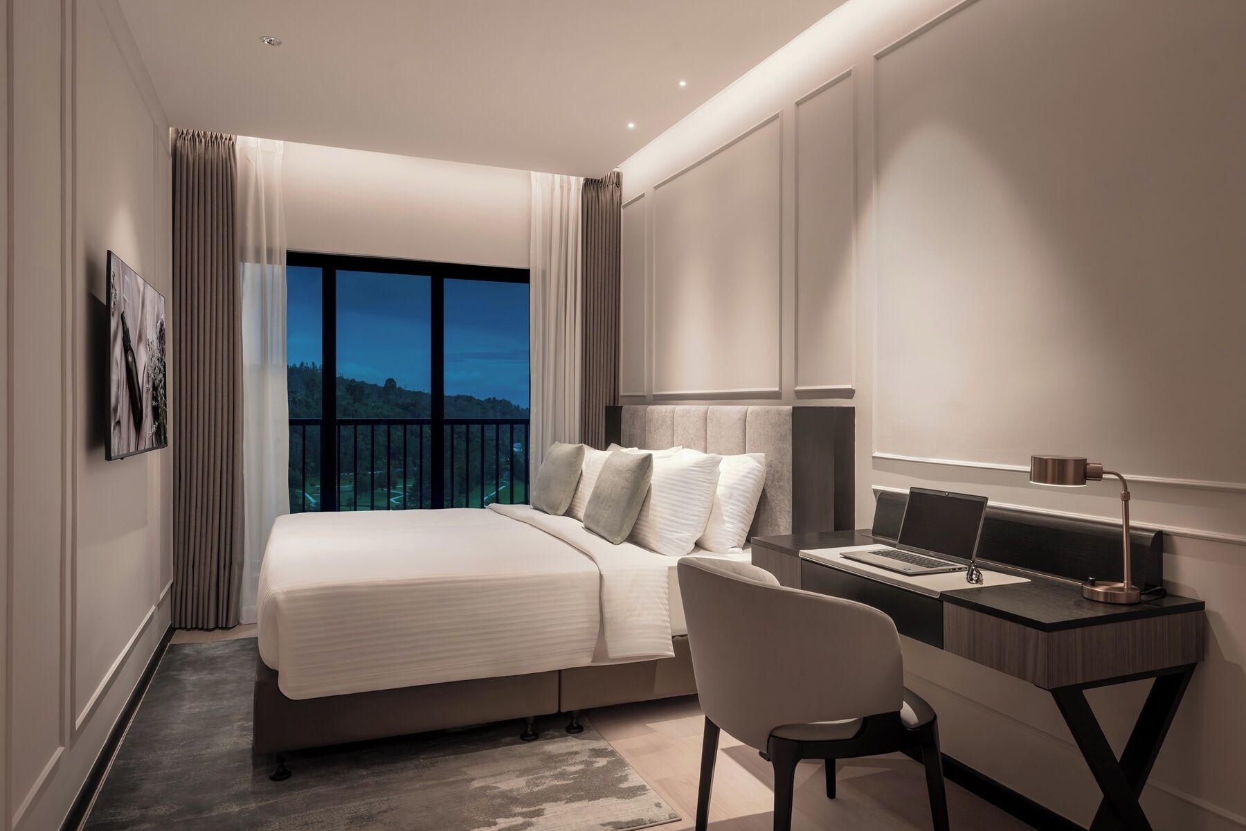 Een moderne hotelkamer met een groot bed, een bureau met een laptop en uitzicht op een landschap door het raam.