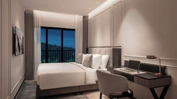 A modern hotel room with a large bed, a desk with a laptop, and a view of a landscape through the window.