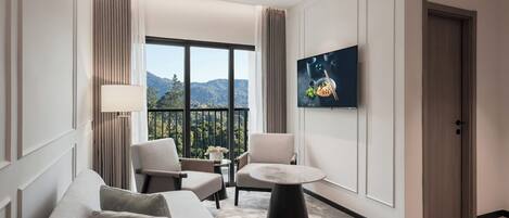 Hotelkamer met een bank, twee stoelen, een klein tafeltje, een televisie en een balkon met uitzicht op de bergen.