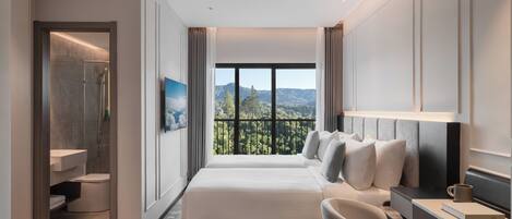 A modern hotel room with a large bed, a desk, a chair, a bathroom, and a balcony with a view of the mountains.