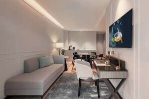 A modern hotel room with a grey sofa, a dining table with chairs, a desk with a laptop, and a TV on the wall. - Oakwood Cameron Highlands (Tanah Rata)