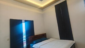 Een slaapkamer met een bed, een plafondlamp en een raam met gordijnen.
