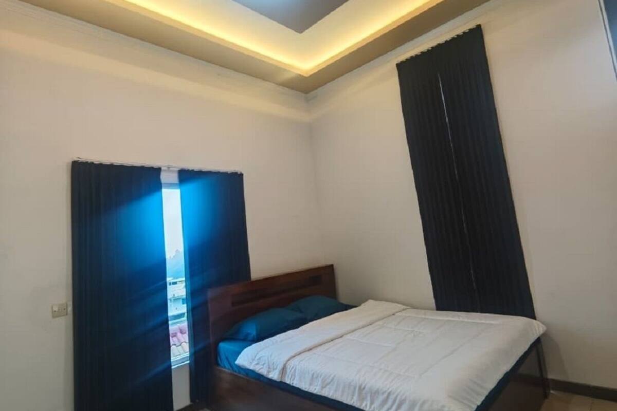 Une chambre à coucher avec un lit, un luminaire au plafond et une fenêtre avec des rideaux.
