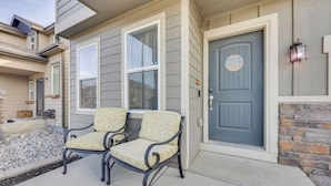 A two-story house with a front porch featuring two chairs and a blue door with a welcome sign.