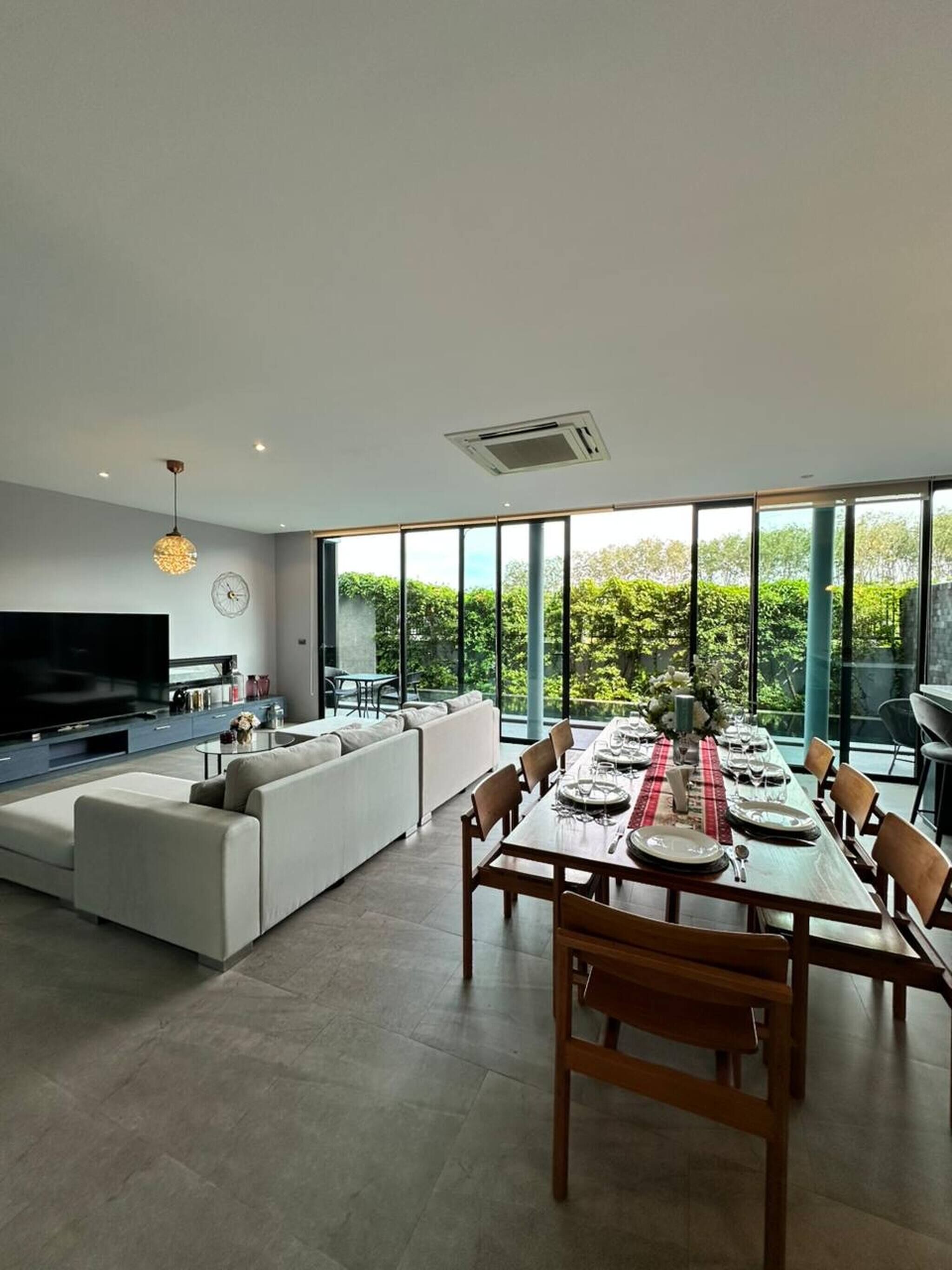 A modern living room with a large TV, a sofa, and a dining area with a table set for six.