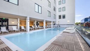 Ein modernes Hotel mit Pool auf dem Dach, Liegestühlen und einer Glasbrüstung.