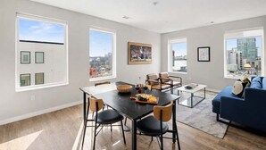 Ein modernes Wohnzimmer mit Essbereich, großen Fenstern und Blick auf die Stadt.