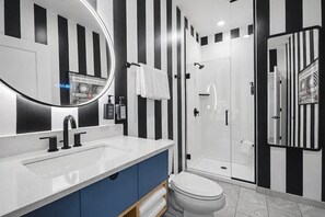 Ein modernes Badezimmer mit einer Wand in Schwarz-Weiß-Streifen, einem großen Spiegel, einem weißen Waschbecken und einer Duschkabine aus Glas.
