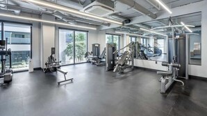 Un gimnasio moderno con diversas máquinas de ejercicio, amplias ventanas y un diseño industrial limpio.