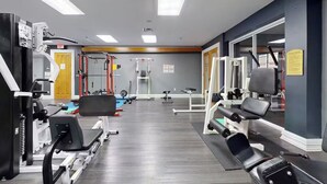 Une salle de sport équipée de divers appareils d’exercice, avec un plancher en bois et une porte jaune à l’arrière-plan.