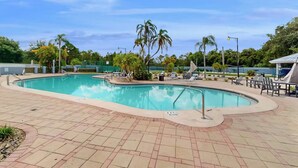 Une piscine avec une terrasse carrelée, des palmiers et des chaises longues.
