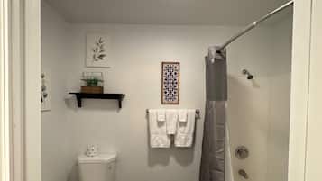 A bathroom with a toilet, a shower, and a bathtub. There are two towels hanging on the wall.