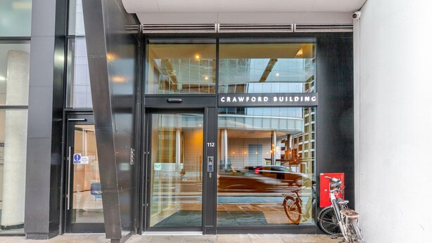 Der Eingang zum Crawford Building mit Glastür, einem sichtbaren Feuerlöscher und einem Fahrrad, das draußen abgestellt ist.