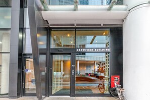 Der Eingang zum Crawford Building mit Glastür, einem sichtbaren Feuerlöscher und einem Fahrrad, das draußen abgestellt ist.