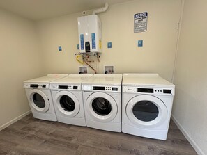Uma lavanderia com quatro máquinas de lavar e secar Whirlpool, um aquecedor de água e um quadro de avisos com as regras da lavanderia.