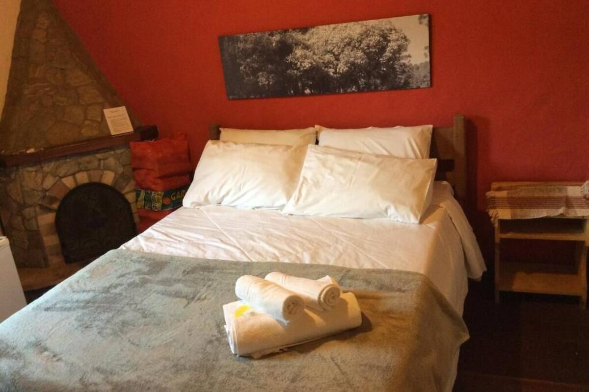 Habitación de hotel con chimenea de piedra, una cama con ropa blanca y un cuadro en la pared.