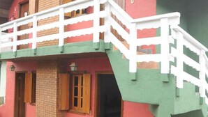 Un edificio a due piani con facciata rossa e verde, un balcone bianco e un camino in mattoni.