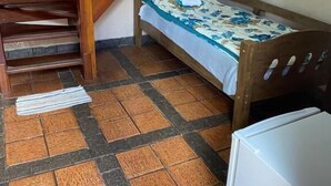 Una stanza piccola con un letto, una scala in legno e un frigorifero.