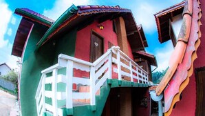 A colorful house with a red and green facade, a white balcony, and a tiled roof. - Villa da Vila (Monte Verde)