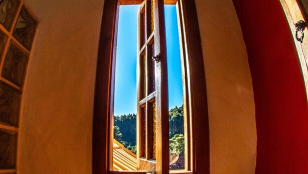 A window with a view of a wooden deck and greenery outside. - Villa da Vila (Monte Verde)