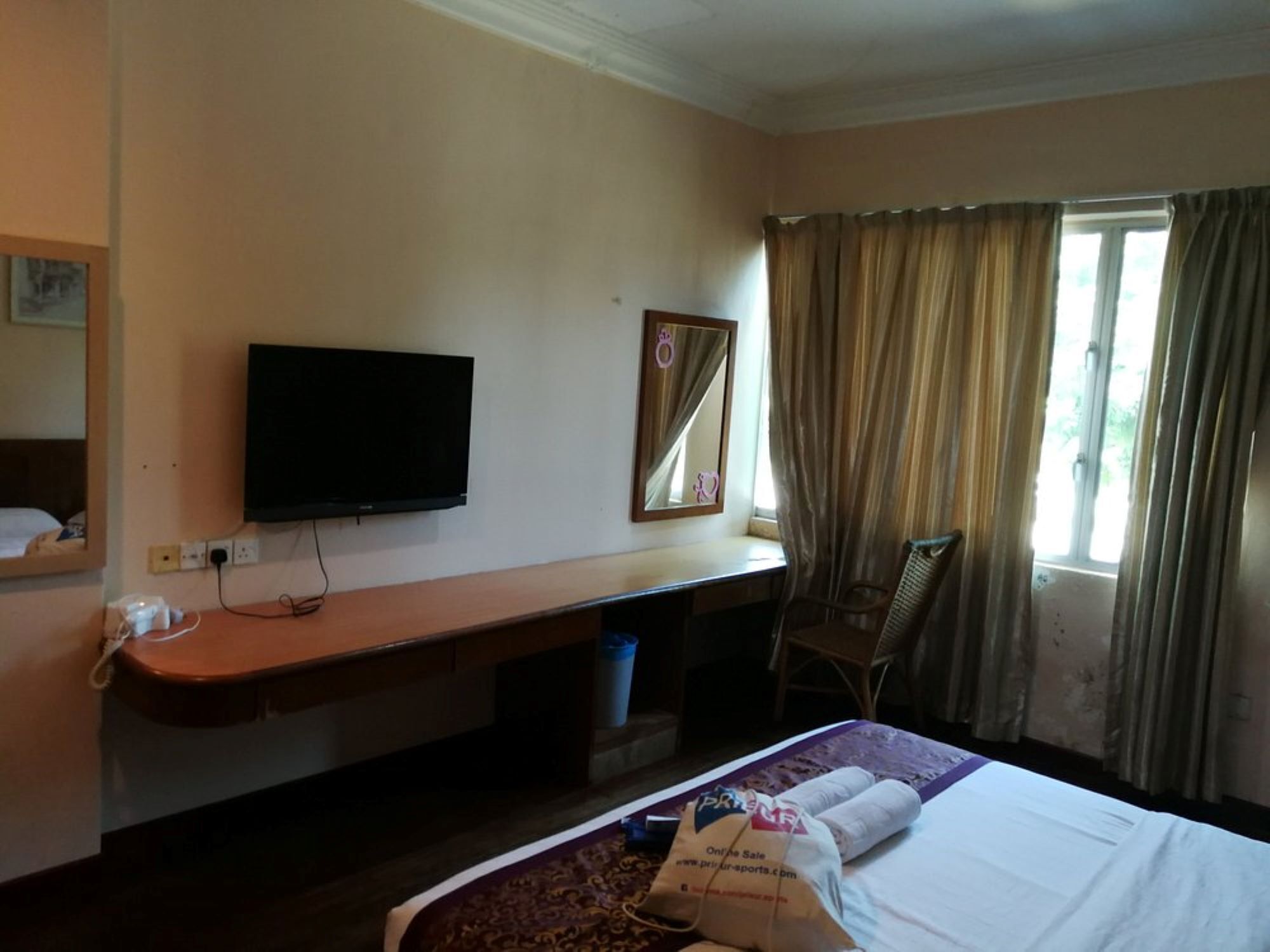 Habitación de hotel con cama, escritorio, silla, televisor y ventana con cortinas.
