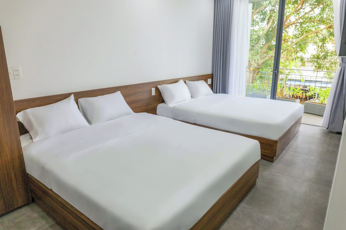 Two single beds with wooden headboards in a hotel room with a large window and a balcony.