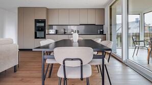 Een moderne keuken met een eethoek, met een grote tafel en stoelen, een inbouwoven en een uitzicht door grote ramen.