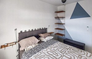 A bedroom with a bed, bedside tables, a bench, and a geometric wall design. - Bel appartement avec terrasse (Mimizan)