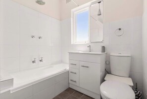 Ein Badezimmer mit Badewanne, Toilette, Waschbecken und Fenster.