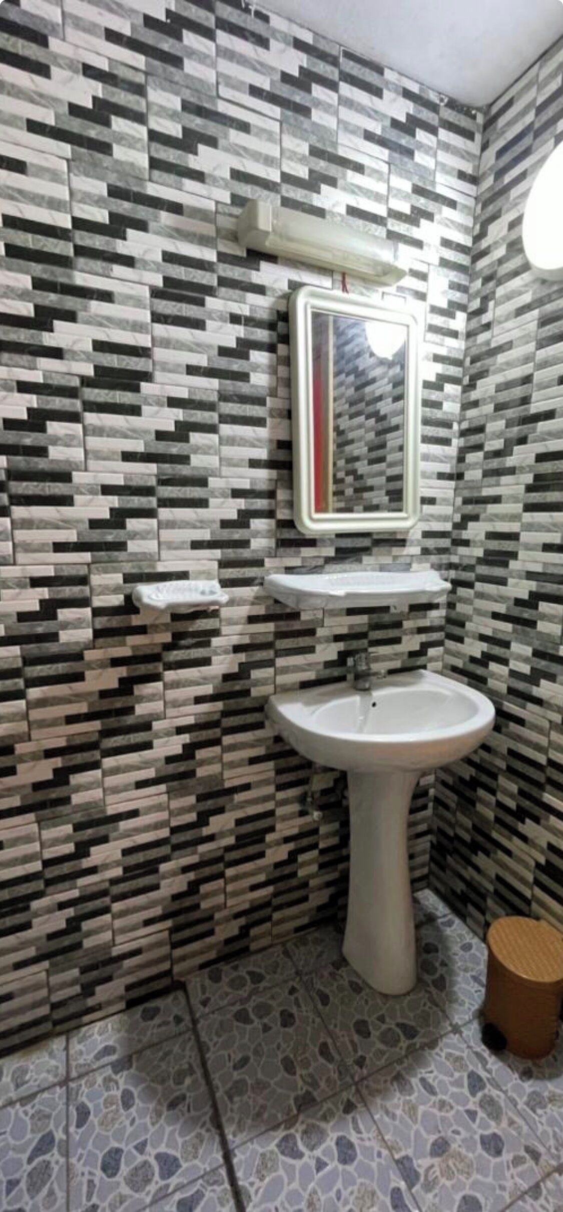 A bathroom with a tiled wall, a pedestal sink, a mirror, and a toilet.