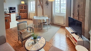 Una sala de estar acogedora con una mesa de comedor preparada para cuatro personas, un sofá cómodo, un televisor y una zona de cocina con microondas y armarios.