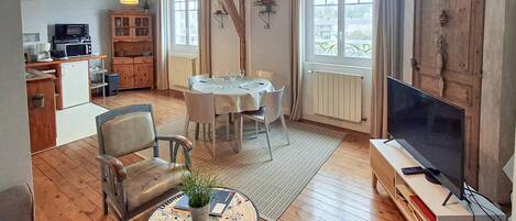 A cozy living room with a dining table set for four, a comfortable sofa, a television, and a kitchen area with a microwave and cabinets.