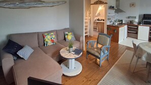 Una sala de estar acogedora con un sofá, una mesita redonda y un sillón. Se ve una escalera que sube a una zona tipo loft.