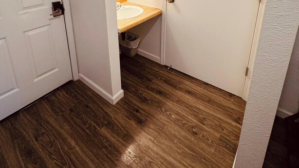 Un baño con suelo de madera, una puerta blanca y una encimera de madera con un lavabo.
