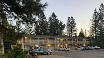 A motel with multiple floors, a parking lot, and a forested backdrop.