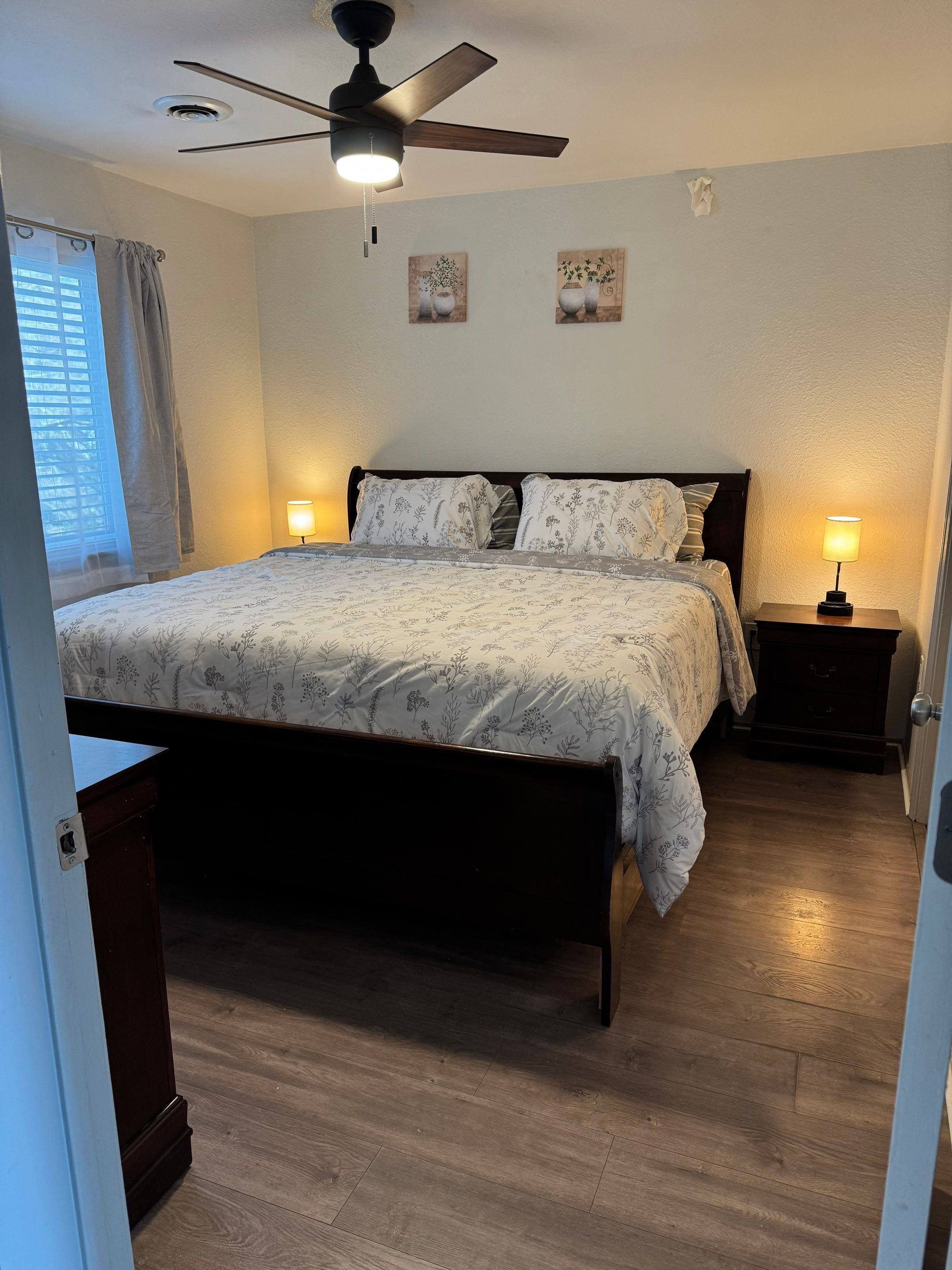A bedroom with a bed, bedside lamps, a ceiling fan, and a window with curtains.