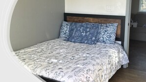 A bed with a floral-patterned bedspread and a blue pillow, a wooden headboard, and a small wall art piece above the bed. - 11 - 1 king, 1 full, 1 queen, 2br, 1ba suite (Challenge-Brownsville)