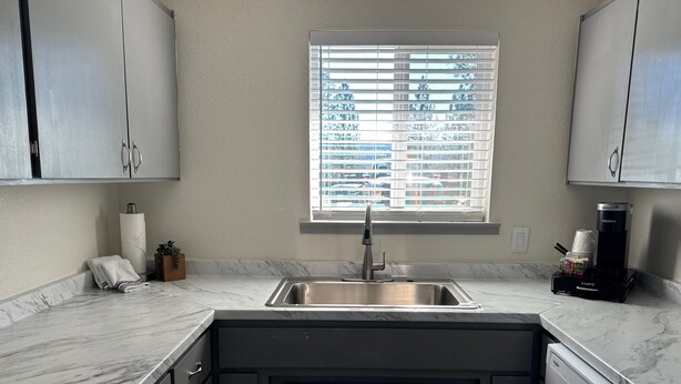 A modern kitchen with a stainless steel sink, marble countertops, and a window with blinds. - 11 - 1 king, 1 full, 1 queen, 2br, 1ba suite (Challenge-Brownsville)